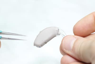 Photo of someone holding a hearing device in one hand and a set of tweezers in the other