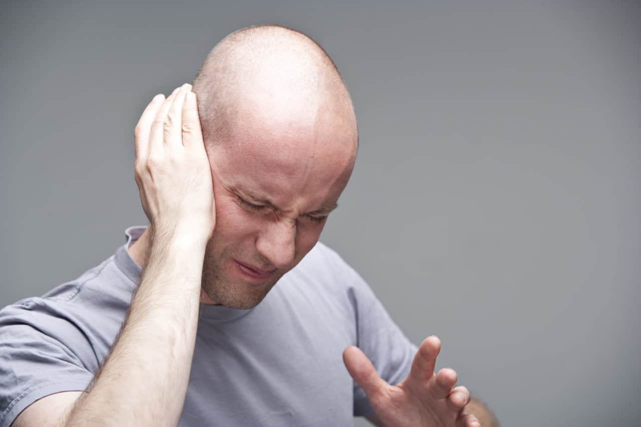 Photo of a person holding one hand up to their ear and wincing in pain