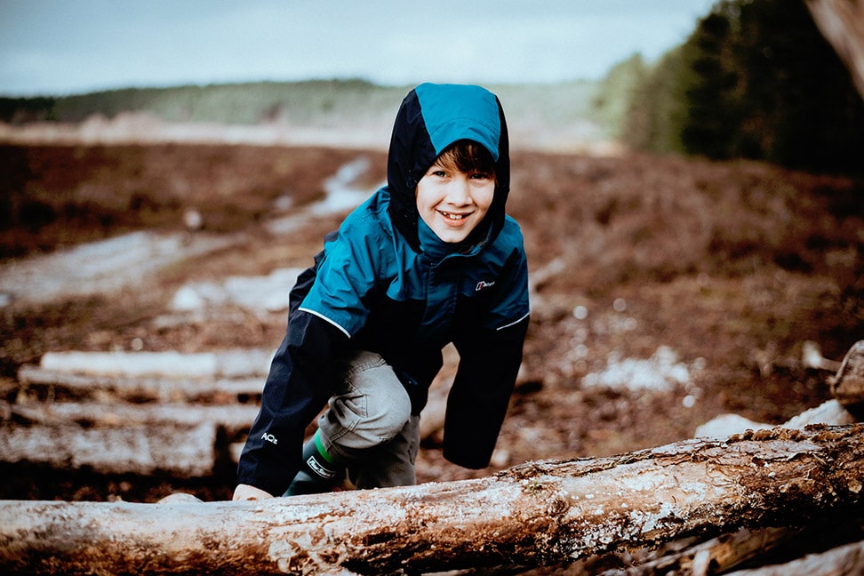 Photo of a boy wearing a jacket and climbing a pile of logs