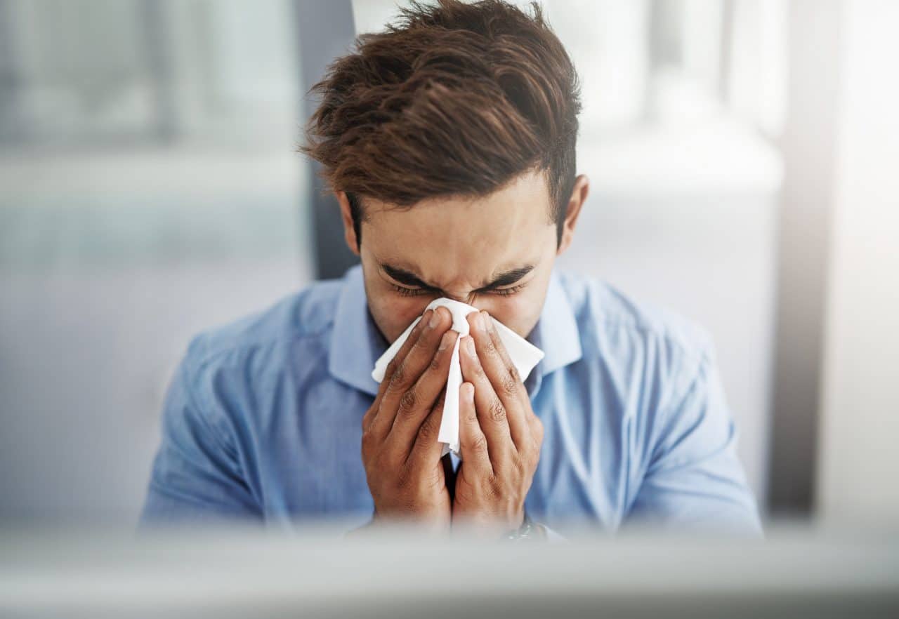 Shot of a young businessman blowing his nose with a tissue at work