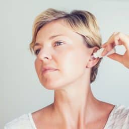 Woman using ear drops in front of gray background