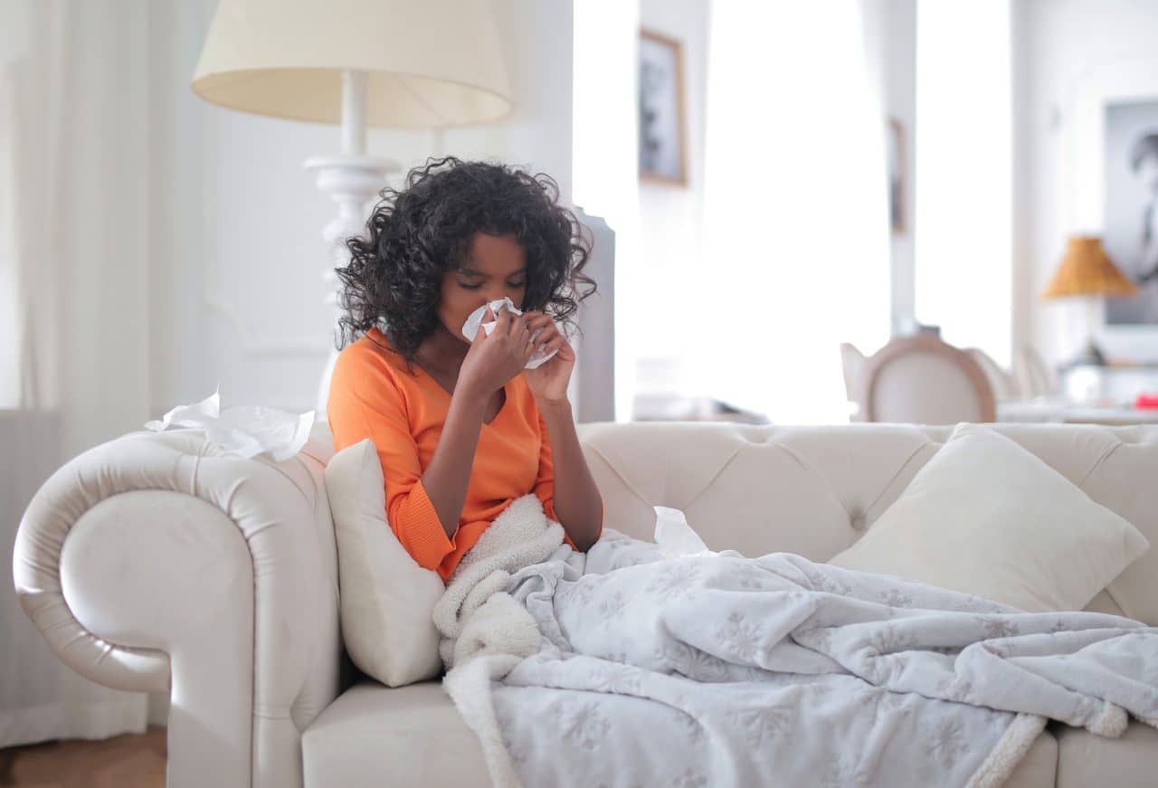 Sick woman blowing her nose and resting on her couch.