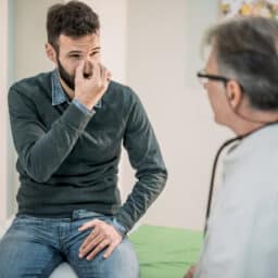 Man talking to his doctor while pinching his nose