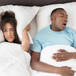 Woman covering her ears with a pillow while her partner snores