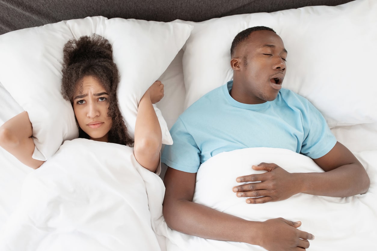 Woman covering her ears with a pillow while her partner snores.