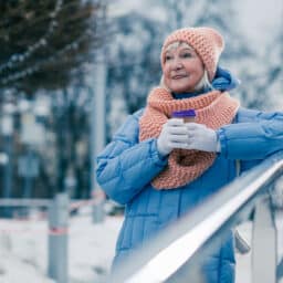 Woman bundled up in a scarf and jacket, holding a warm cup of cocoa in the snow.