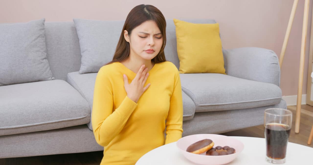 Woman experiences silent reflux after drinking a caffeinated beverage and eating sugary food.