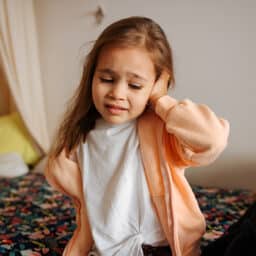 Small child with an ear infection holds her ear in pain.
