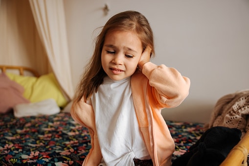 Small child with an ear infection holds her ear in pain.