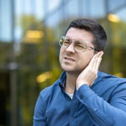Wan with ear pain holds his ear and grimaces.